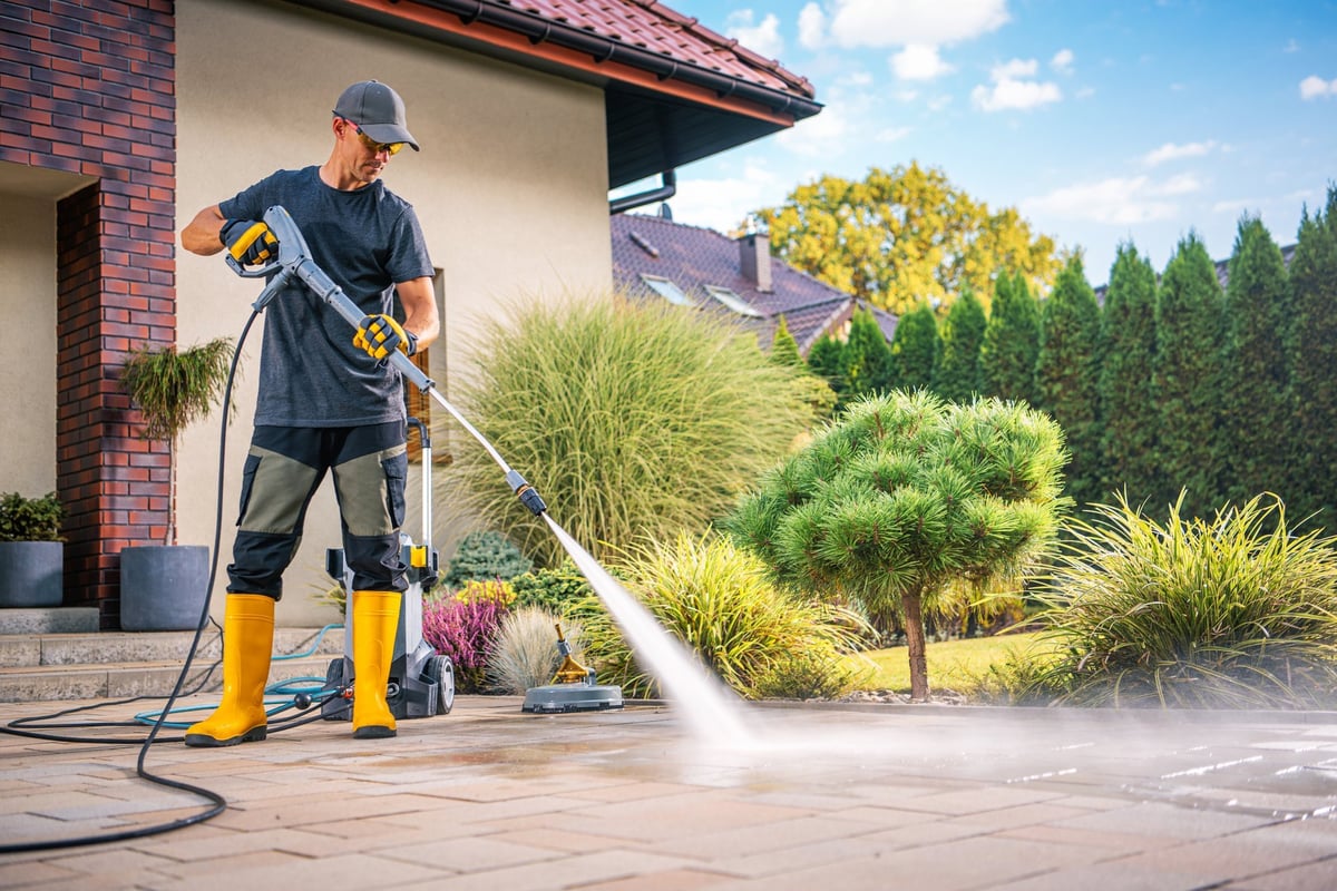 A man power washing a patio in a sunny garden