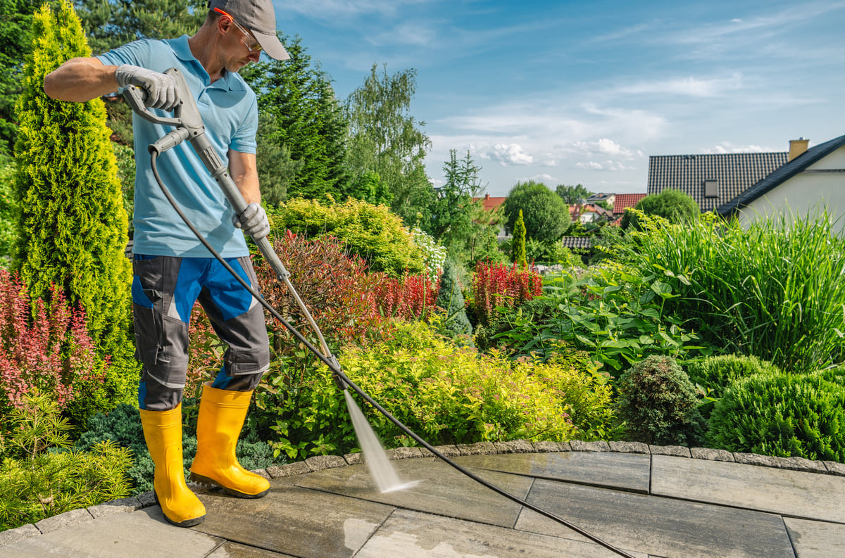 A professional presses washes a patio surrounded by vibrant greenery and flowers