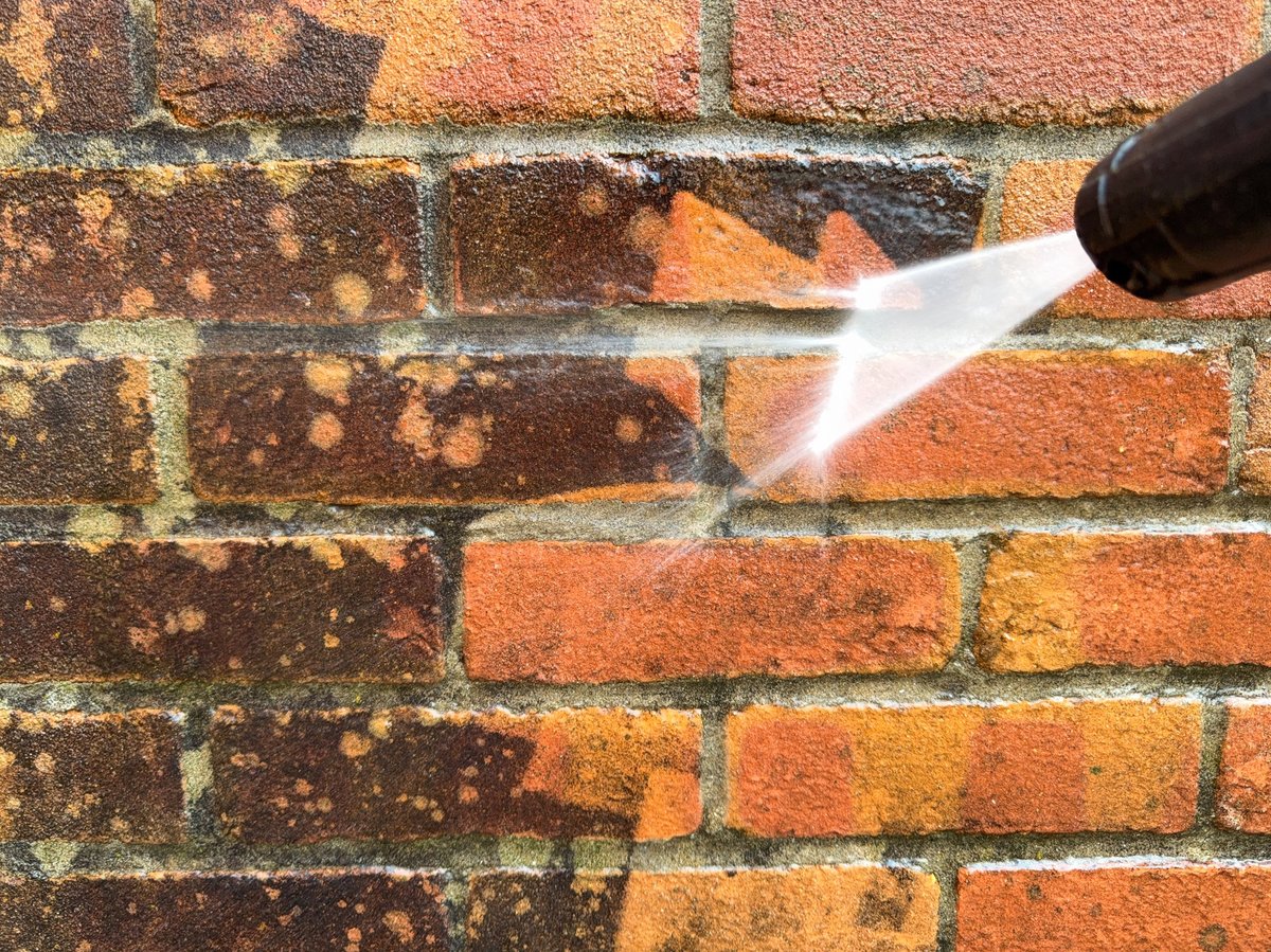 A pressure washer removing dirt from dirty bricks on a garden wall