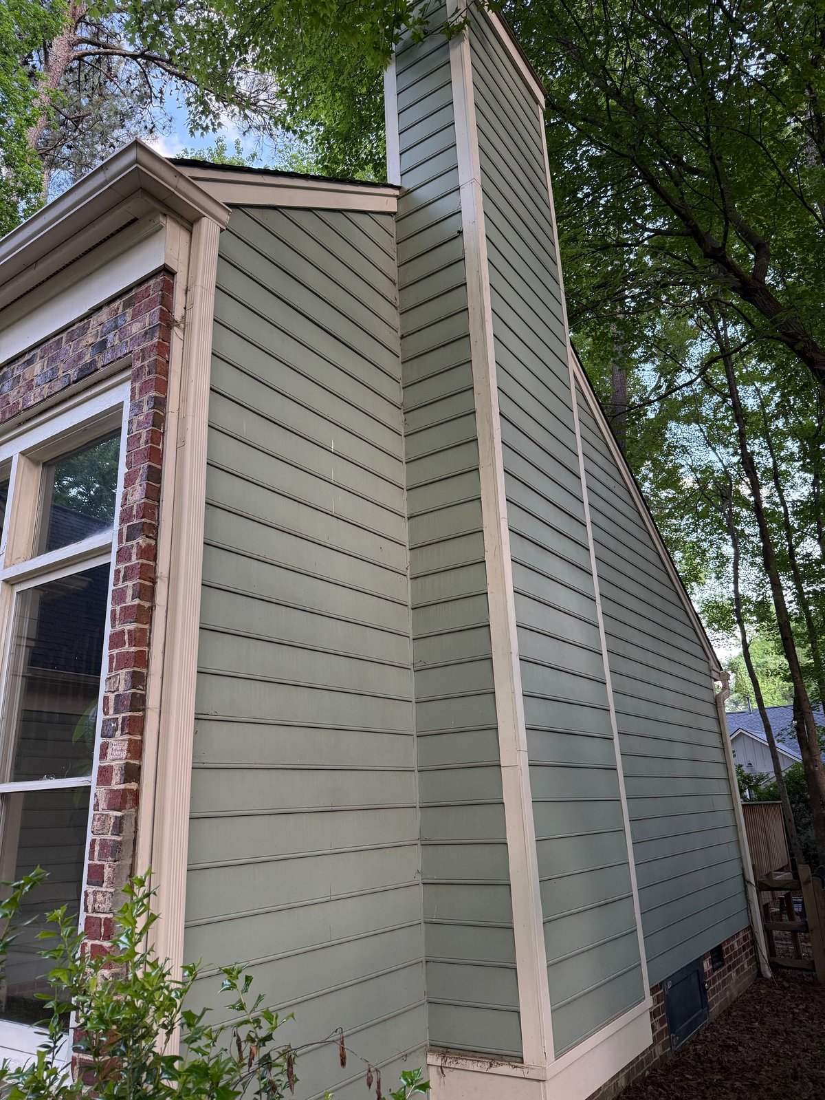Modern house exterior with gray horizontal siding, brick chimney, and surrounded by green trees