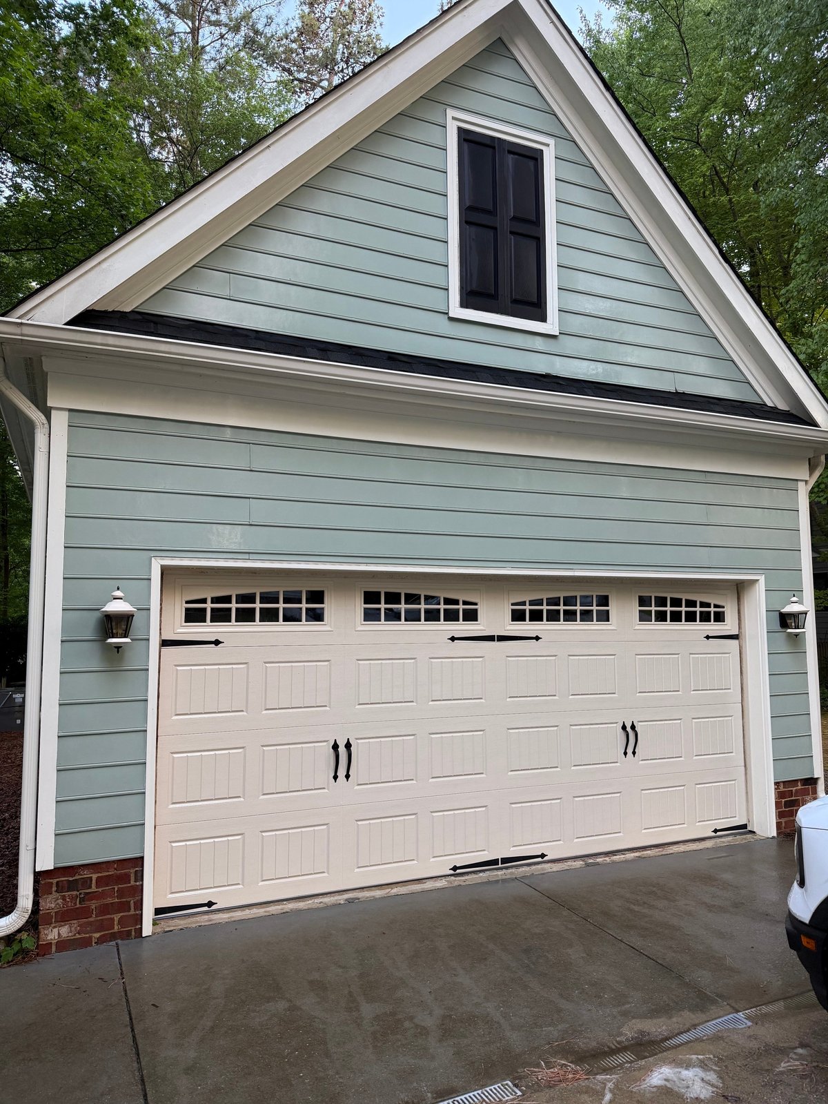 Modern two-car garage with cream-colored doors and light blue siding, featuring a peaked roof with a small upper window.