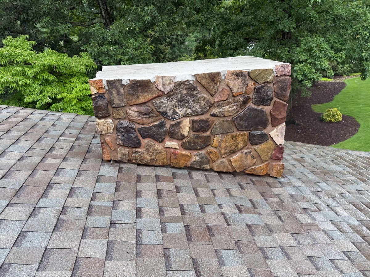 Stone and marble outdoor bench on a patterned paver patio with green landscaping and trees in the background