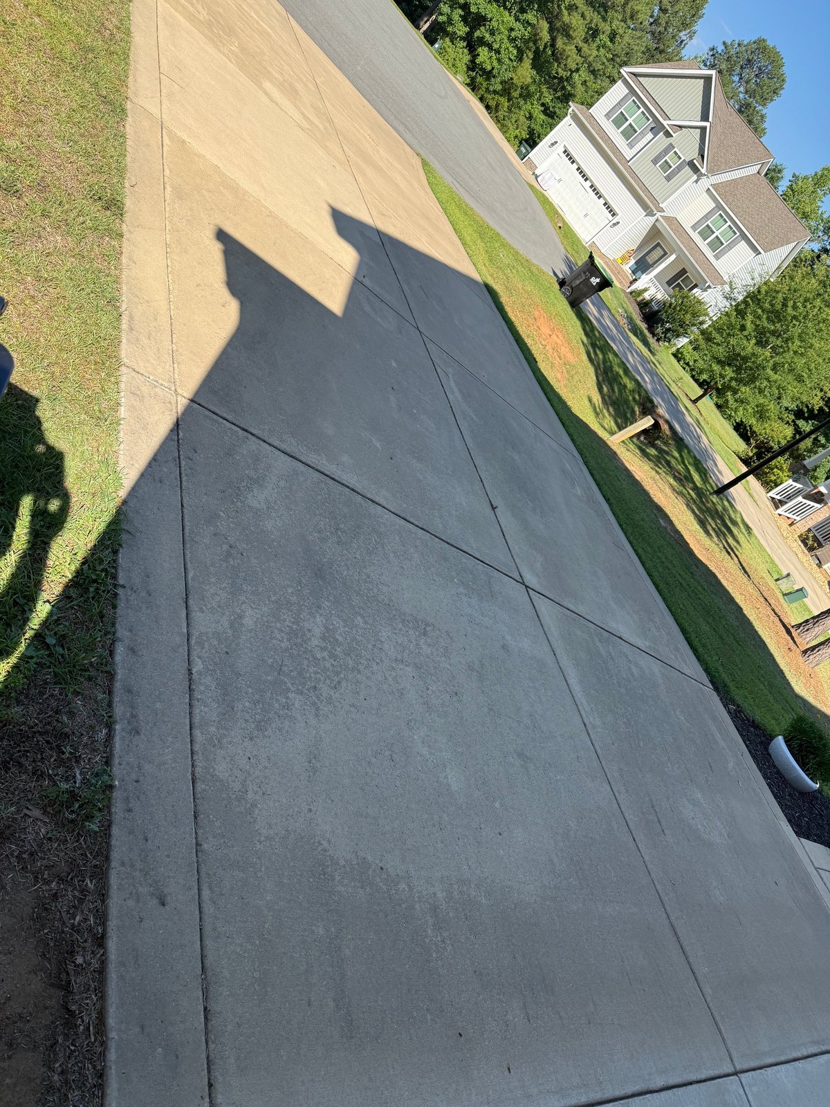 Aerial view of a driveway with shadows cast by a person and structure, showing a residential home with landscaping