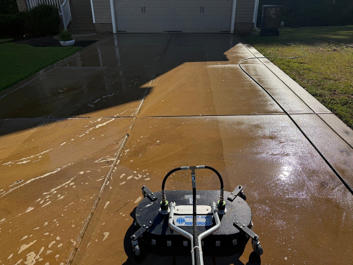 Flooded driveway with muddy water and a riding mower in the foreground near a residential garage