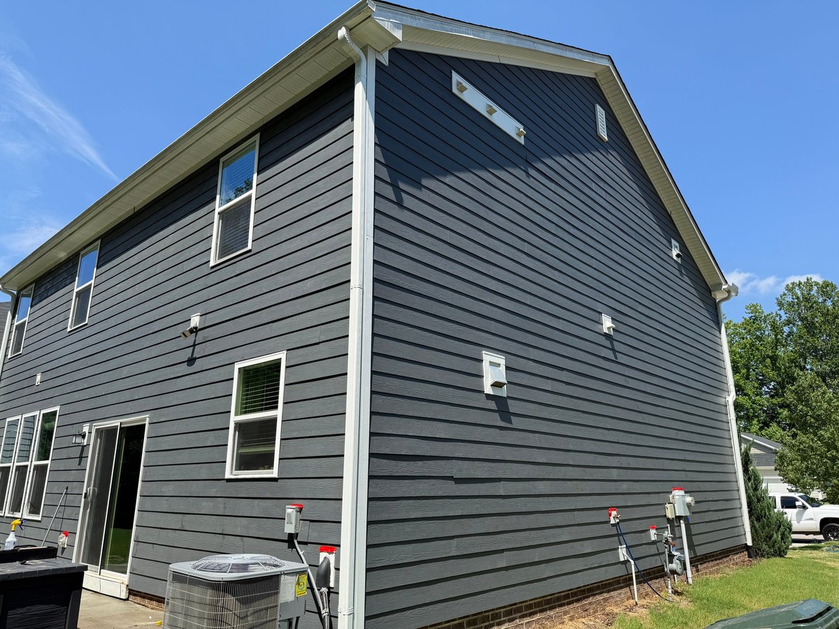 Two-story gray modern house with horizontal siding, multiple windows, and a peaked roof under blue sky