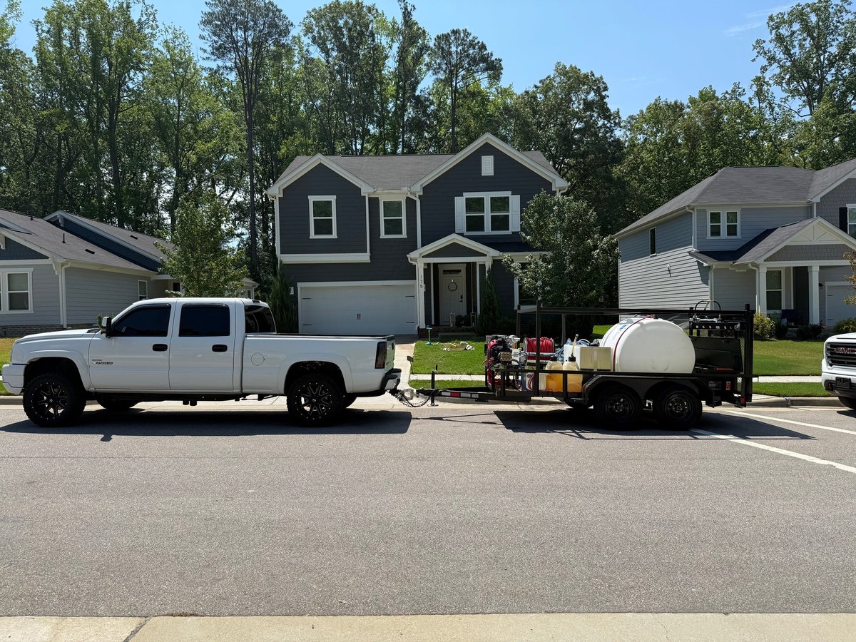 White pickup truck parked in residential street with utility trailer and dark gray two-story house in background