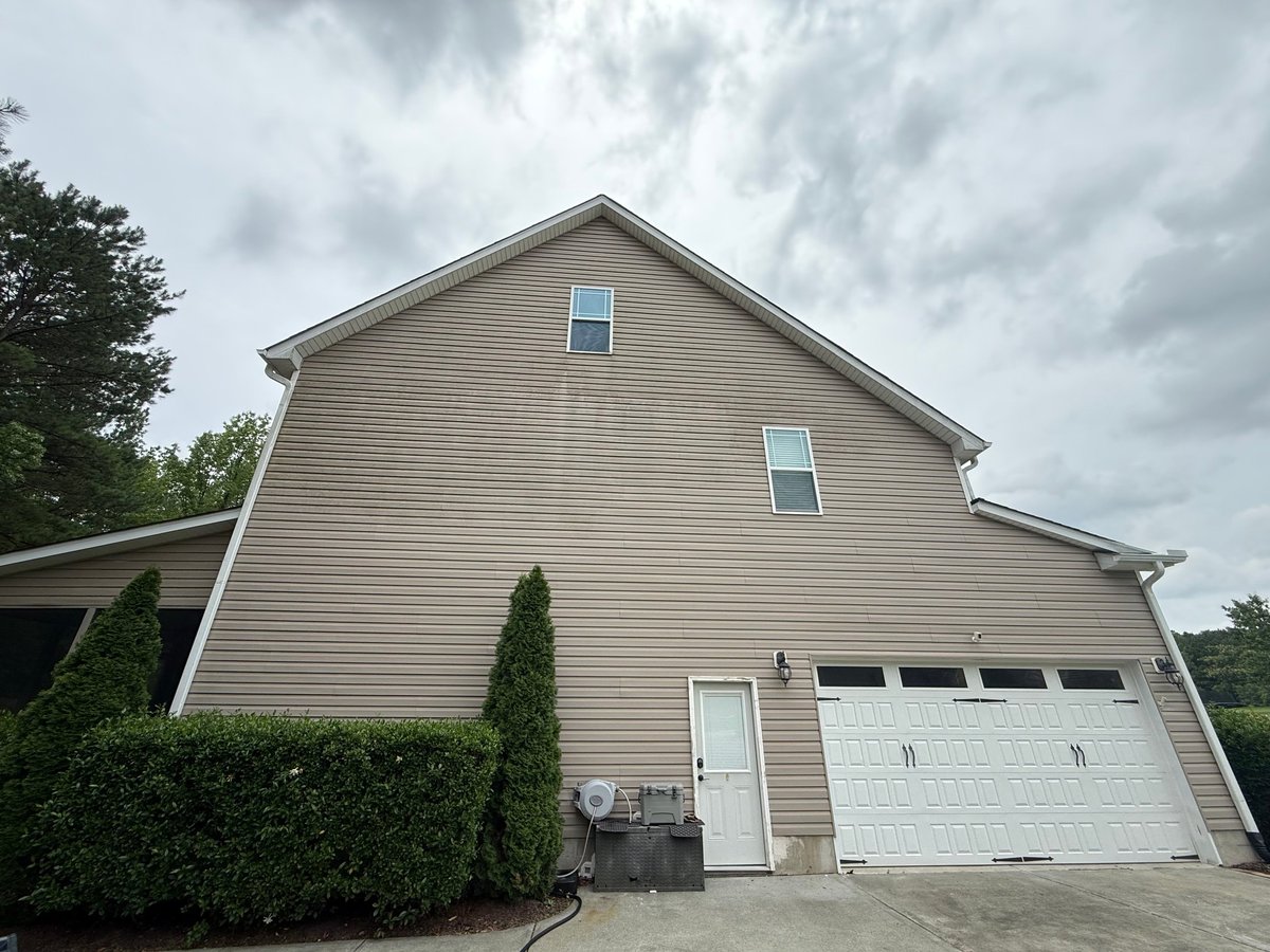 Two-story beige house with white garage door, green shrubs, and cloudy sky