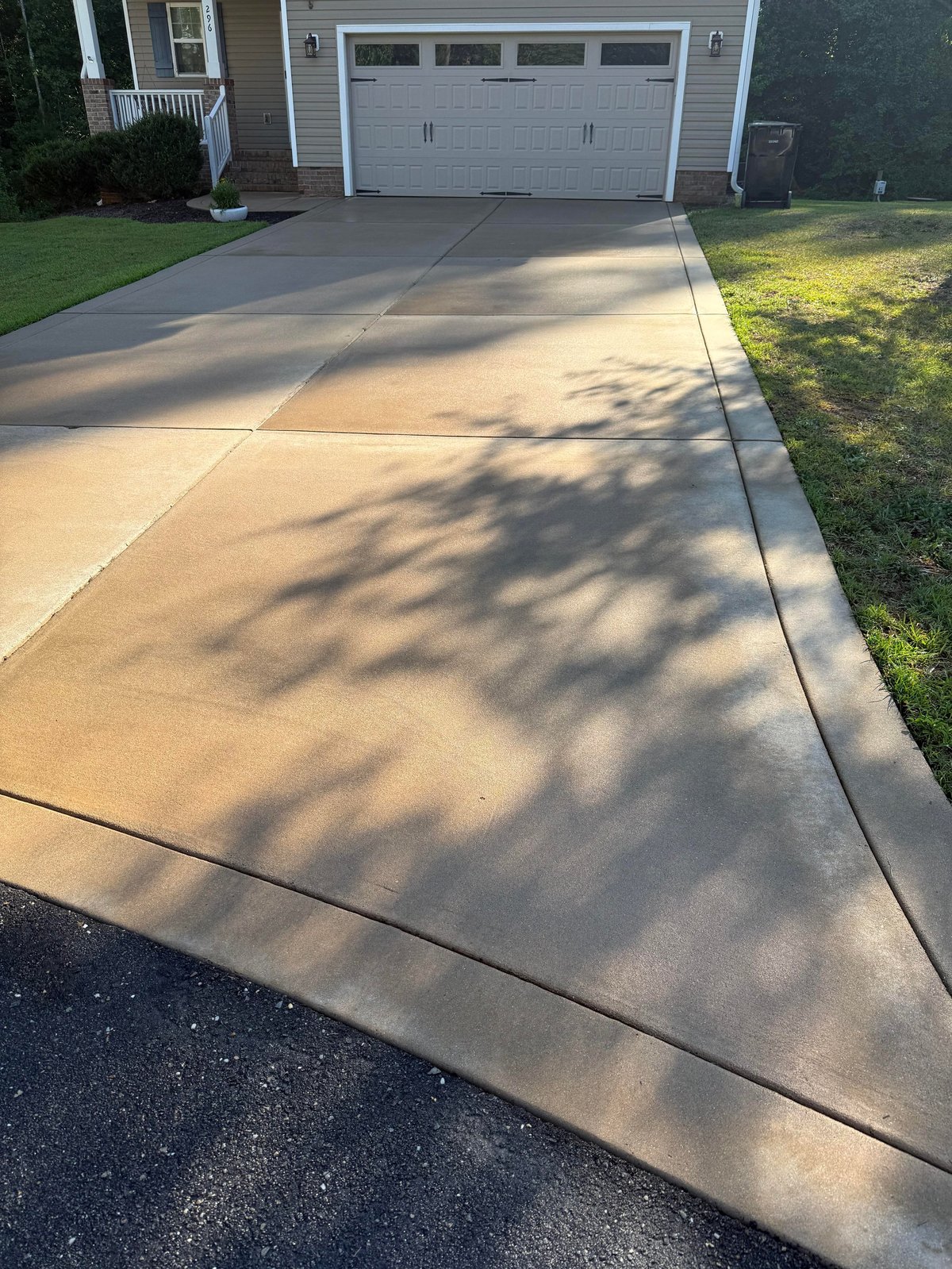 Concrete driveway with tree shadows in front of a two-car garage and house with green lawn on the sides