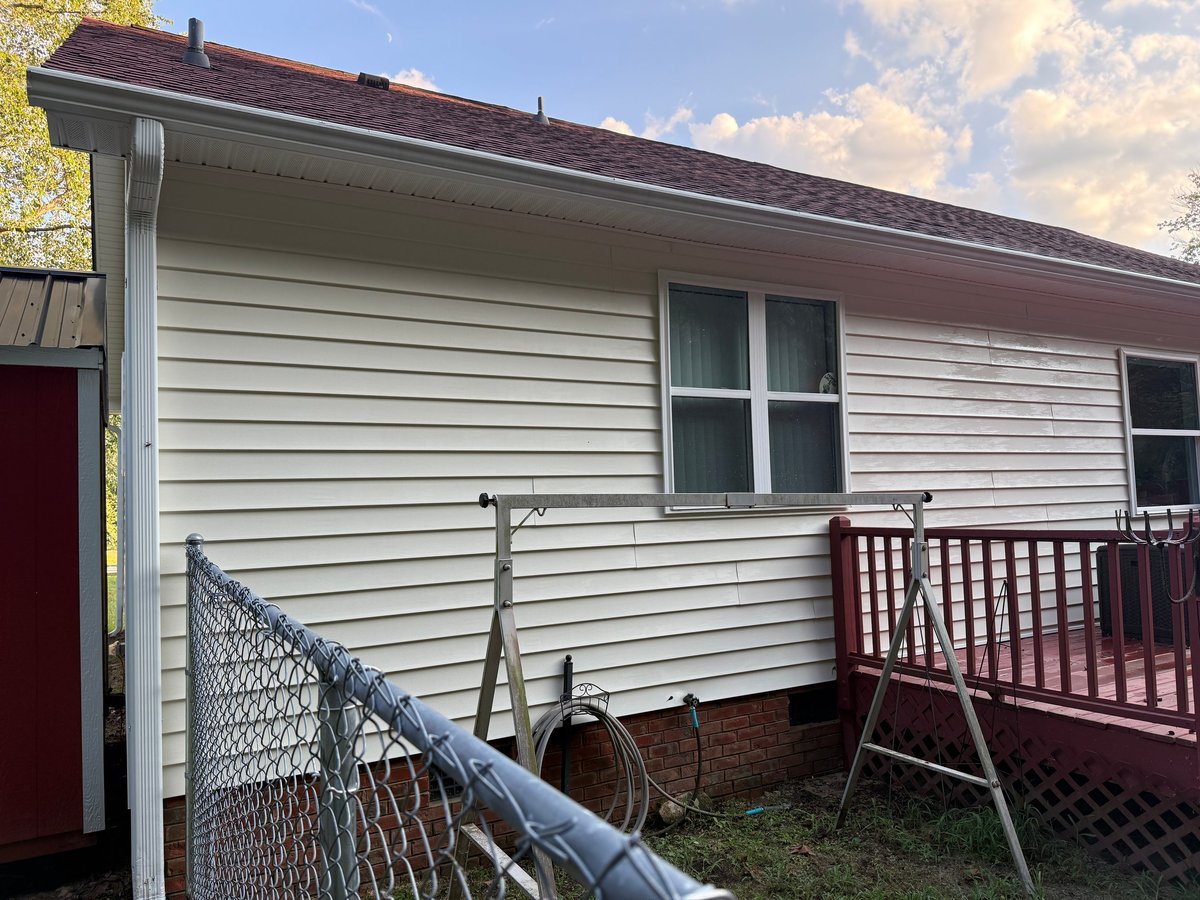 Single-story white vinyl siding house with dark roof, deck, and fence under cloudy sky